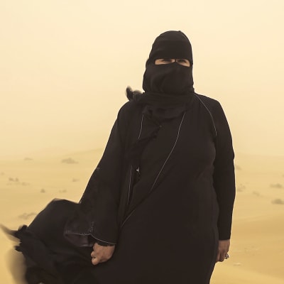 Hissa Hilal står ute i öknen under en sandstorm.