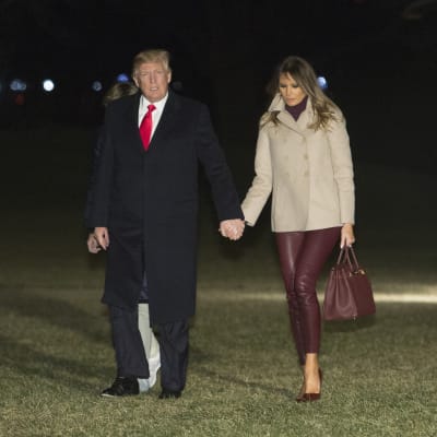 Yhdysvaltain presidentti Donald Trump ja Melania Trump kävelevät käsikädessä nurmikolla.
