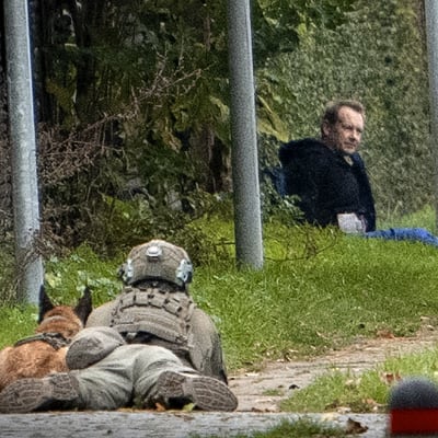 Mies koira koira vieressään vahtii maassa istuvaa Peter Madsenia.