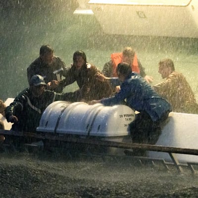 Ihmiset yrittävät laskea pelastuslauttaa myrskyssä. Laiva on kallistunut niin että parras hipoo vettä.