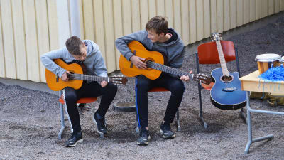 Två pojkar sitter utomhus och spelar gitarr.