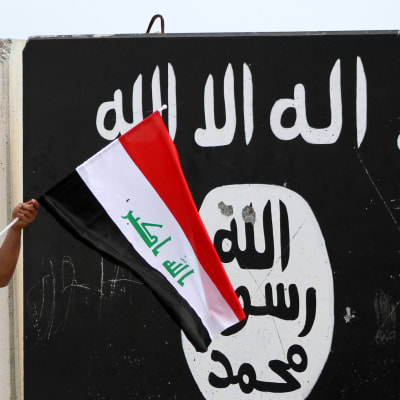En hand som håller i Iraks flagga framför en svartvit IS flagga.