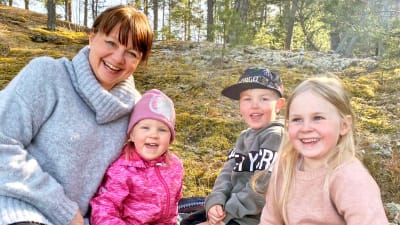 Åsa Rosenberg sitter på en klippa tillsammans med barnbarnen Luna, Jasper och Nova. 
