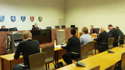 Sex personer sitter på rad i en rättegångssal framför en domare, åklagare och ett rättegångsbiträde.