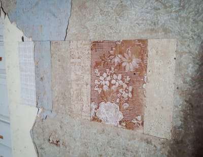 Små rutor med olika sorters slitna tapeter på en vägg.
