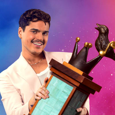 Melodifestivalens programledare Oscar Zia i vit kostym mot färggrann bakgrund och med pokal i famnen.