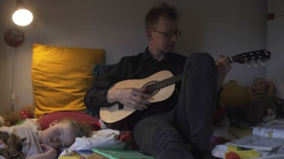 Man spelar gitarr för somnande barn