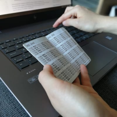 En hand håller i ett nyckelkort för nätbanken ovanför ett tangentbord. Den andra handen knäpper på tangenterna.