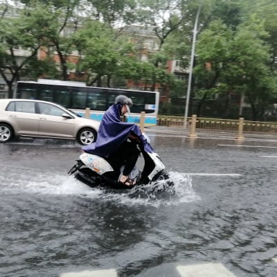 Moottoripyöräilijä ajaa tulvaveden peittämällä tiellä.
