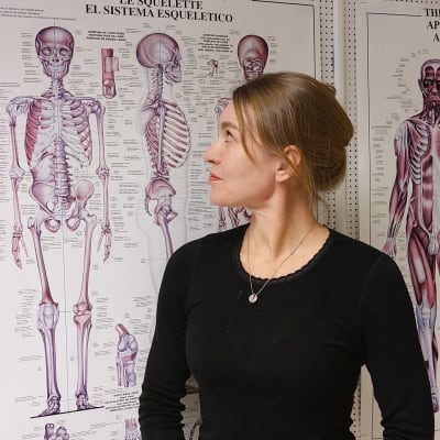 kvinna framför anatomisk affisch av skelett