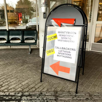 en skylt utomhus som med pilar och klar färg pekar att mottagning för luftvägsinfektioner är till vänter om skylten