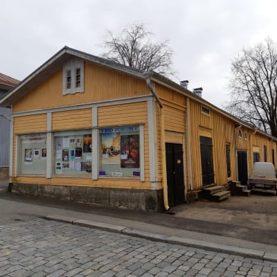 Ett gult uthus vid en gågata. På fasaden finns reklam för biograf och olika föreninger.