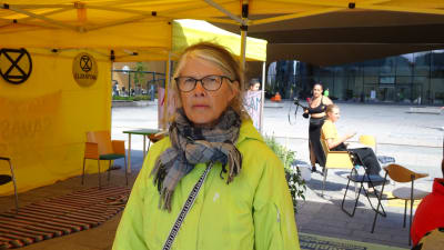 Eeva Kaila i en ljusgrön rock och halsduk inne i ett gult tält. Hon har glasögon på sig.  