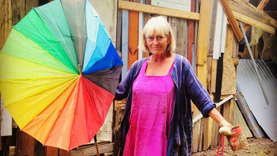Antonia Ringbom, en äldre kvinna står på inspelningsplatsen med ett färggrannt paraply i handen.