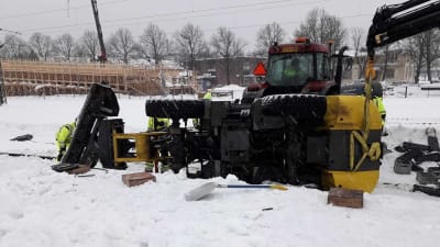 Plogbil ligger över spår och ett annat fordon försöker lyfta upp den. Myckey snö på marken.