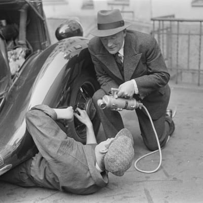 Radioreporter Alexis af Enehjelm intervjuar en man som fixar en bil, 1930-tal