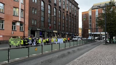 En grupp människor i reflexvästar går längs en gata, bär på banderoller.