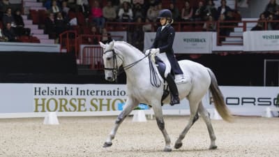 Dressyrryttaren Jenni Rintala sitter iförd dressyrdräkt på sin häst Nk Unique. Fotot är taget i manegen under tävling på Helsinki International Horse Show 2016.