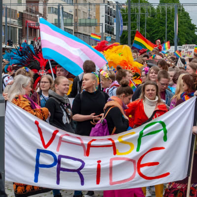 Ett pridetåg med folk, banderoller och regnbågsflaggor.