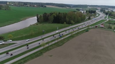 Luftfoto av hundratals motorcyklister som kör längs en riksväg förbi åkrar och en älv.