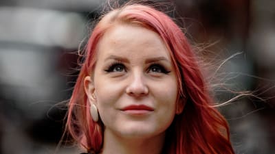 Hilla Kopakkala seisoo kadulla lähikuvassa, katsoo ylöspäin ja hänen hiuksensa heiluvat tuulessa.