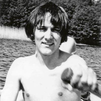 Toimittaja Kari Lumikero soutaa venettä nuorena miehenä, ilman paitaa ja Beatles-tukassa, Mälarenjärvellä Ruotsissa