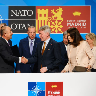 Mevlut Cavusoglu och Pekka Haavisto skakar hand efter förhandlingarna i Madrid. I bakgrunden bland andra Recep Tayyip Erdogan.