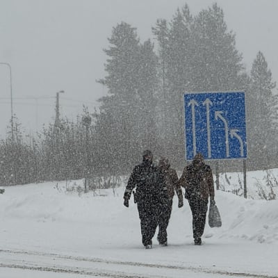 Tre personer går i ett snöigt landskap.