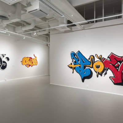 Tuftattuja, graffitia jäljitteleviä ryijyjä taidegallerian seinällä.