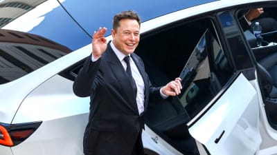 Elon Musk vinkar och ler medan han går in i en bil.