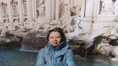 Författaren Susanne Ringell stående med armarna i kors framför fontänen Fontana di Trevi i Rom. 