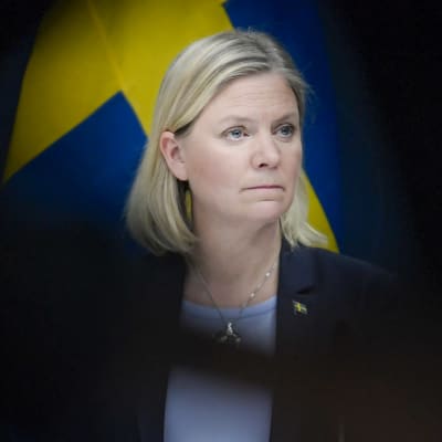 Magdalena Andersson tittar åt sidan. I bakgrunden syns Sveriges flagga.