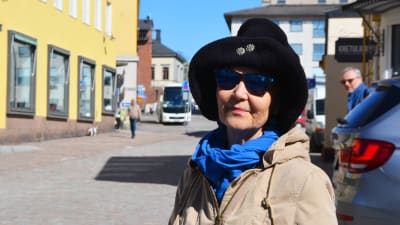 En dam i hatt och solglasögon står i Gamla stan i Borgå.