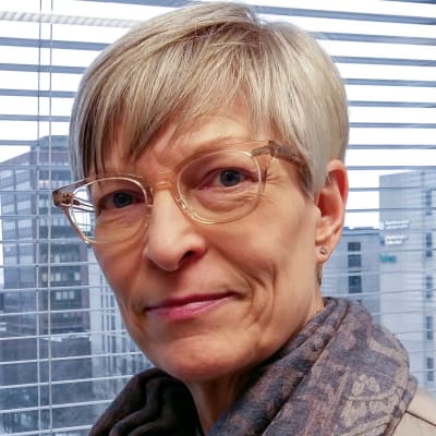 Kirsi Pimiä står framför ett fönster. Hon är Diskrimineringsombudsman i Finland.