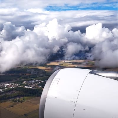 Lentokoneen ikkunasta nähtynä turbiini, maata ja pilviä.