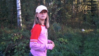 Kymmenvuotias Laura Hovilainen seisoo metsikössä ja katsoo kameraan.