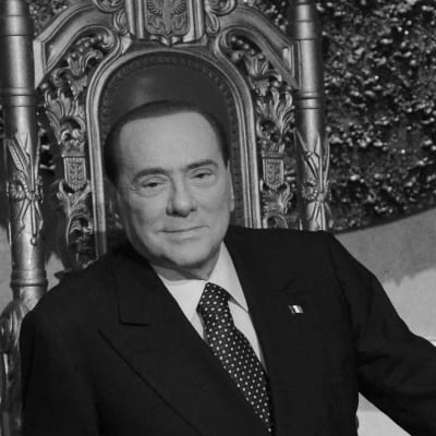Italiens före detta premiärminster Silvio Berlusconi sitter på en tron. Bilden är svartvit.