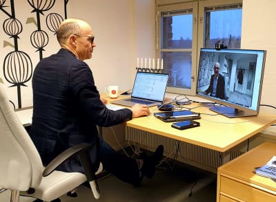En man sitter på ett kontor framför ett skrivbord. Man ser hans datorskärm där han själv är i bild.