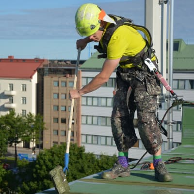 Antti Tervo står på ett sjuvåningshus i Vasa och målar taket.