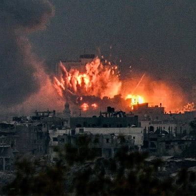 En stor explosion lyser upp en mörk himmel och sönderbombade byggnader.