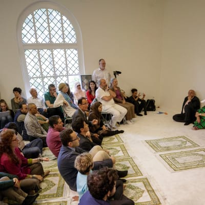 Kuvassa  moskeijan perustaja Seyran Ates ja joukko rukoilijoita, niin miehiä kuin naisiakin, vaaleassa, kauniissa rukoushuoneessa.