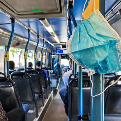 Kertakäyttöinen maski roikkuu bussin tangossa.
