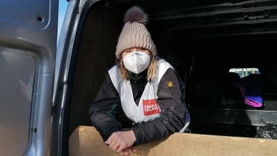 En kvinna klädd i vinterkläder och munskydd tittar ut från en skåpbil.