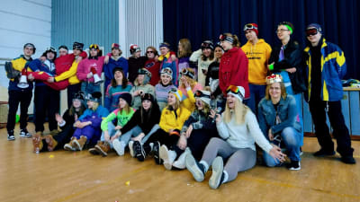 Ungdomar med skidglasögon och mössor inomhus i en skolas festsal/gymnastiksl. Det är penkis i Virkby gymnasium.
