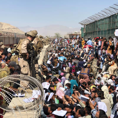 Finländska soldater står på en mur på Kabuls flygplats. På marken står en större folkmassa.
