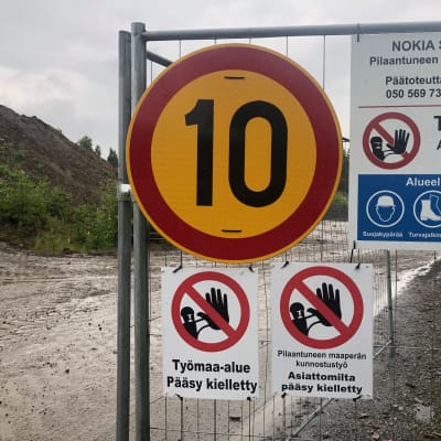 Työmaa-aita, johon on kiinnitetty 10 kilometrin nopeusrajoitusmerkki ja työmaa-alueesta kertovia merkkejä.