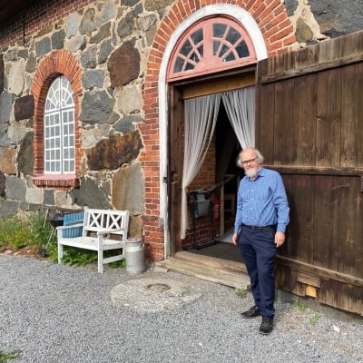 Mies seisoo vanhan kivinavetan oviaukossa ja hymyilee.