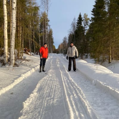 Två män på en skogsväg i vintrigt landskap. 