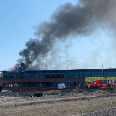 Kuvassa Riihikallion koulu Tuusulassa, jonka vasemmalta puolelta nousee sankkaa mustaa savua. Käynnissä on rakennuspalo.