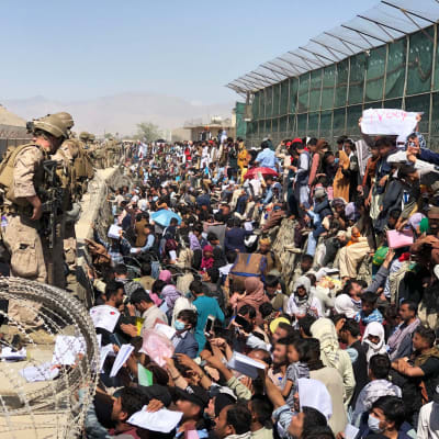 Finländska soldater står på en mur på Kabuls flygplats. På marken står en större folkmassa.